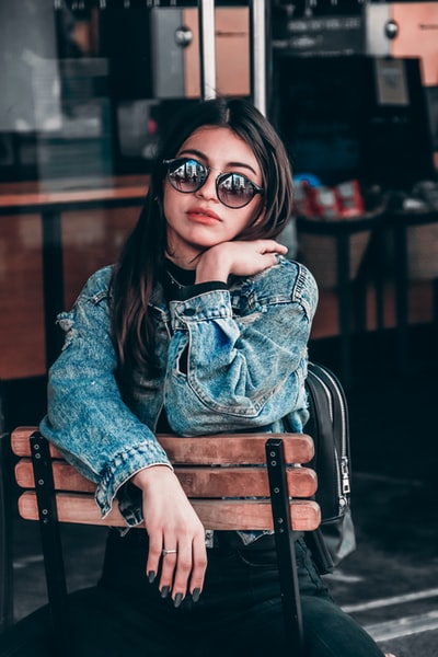 Dressed in blue denim jacket woman sitting on a brown wooden chair
